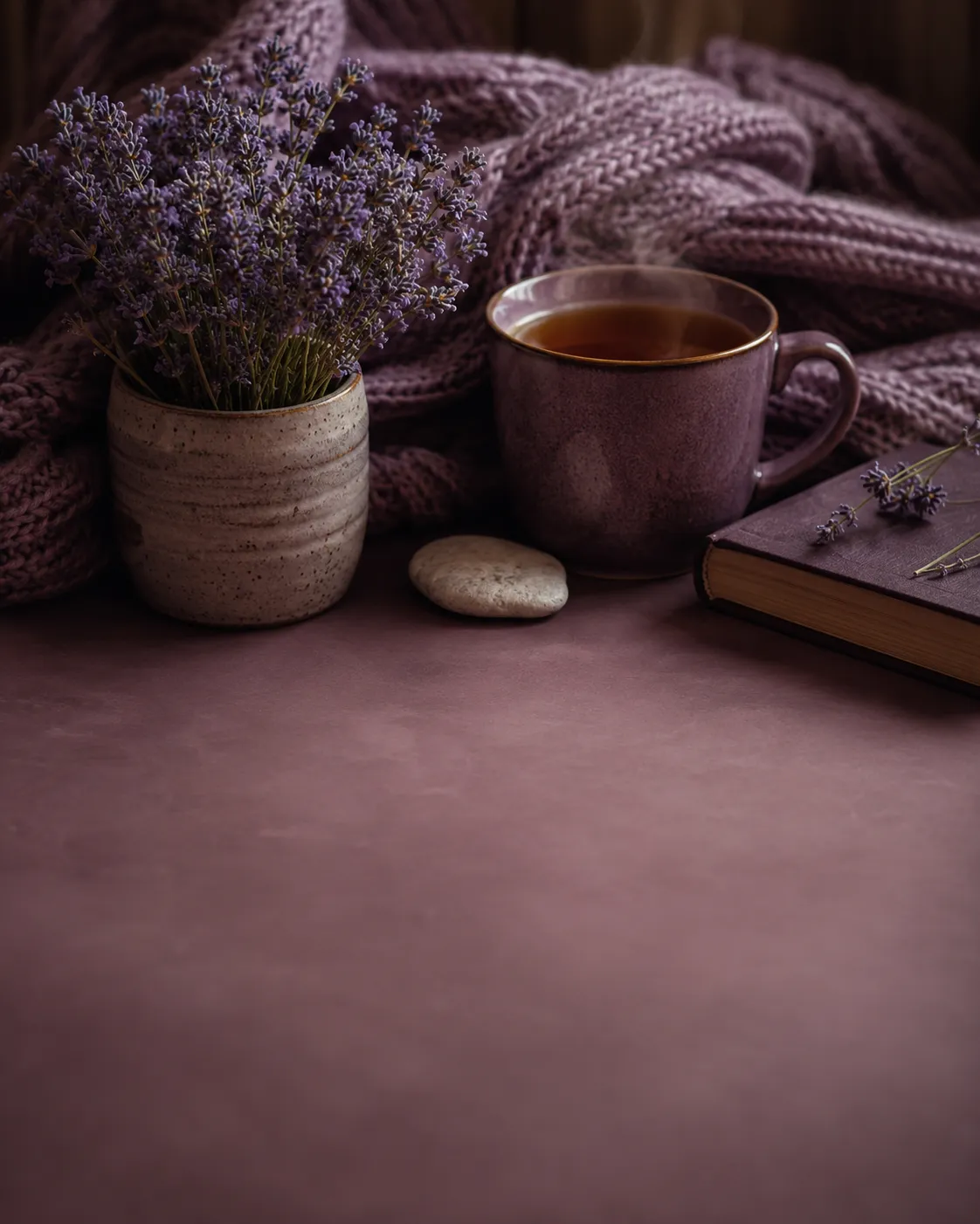Un pot de lavande, une tasse de the et un plaid en maille sur une table, dans une ambiance douce et feutree.