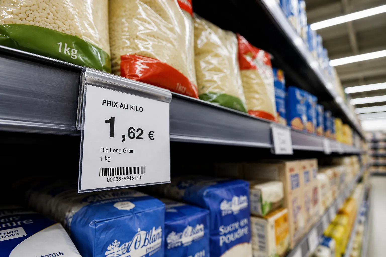 Une etiquette prix au kilo affichant 1,62 € pour du riz, clipsee sur un rayon de supermarche garni de feculents, sous la lumiere artificielle du magasin.